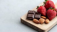 Fresh ripe strawberries with dark chocolate squares and almonds on wooden cutting board against light background, healthy dessert ingredients.