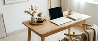 Minimalist home office with wooden desk, open laptop, coffee maker, dried flowers, and cozy chair in a bright Scandinavian-style interior.