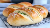 Fresh baked bread rolls with herbs on cooling rack, golden brown crust and soft texture, sprinkled with flour, close-up view of homemade bakery.