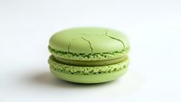 Green macaron with cracked shell on white background, French pastry dessert for bakery menu design and culinary projects.