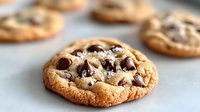 Fresh baked chocolate chip cookie with melted chunks and golden crispy edges on light background, selective focus on gooey center. Perfect for food blogs.