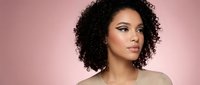 Young African American woman with curly hair and natural makeup on pink gradient background for beauty and skincare campaigns.