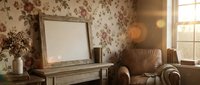 Cozy vintage living room interior with floral wallpaper, leather armchair, wooden console table, blank picture frame and warm natural lighting.