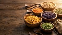 Assorted legumes and grains in wooden bowls on rustic table. Colorful lentils, beans, chickpeas and cereals for healthy cooking and nutrition concepts.