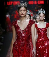 Young Asian woman in sparkling red sequined evening gown and crystal crown walks runway with models in matching dresses against dark background. Fashion show glamour.