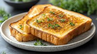 Golden-brown toasted bread slices garnished with fresh herbs and butter on ceramic plate, close-up view with soft natural lighting and shallow depth of field.