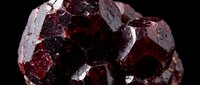 Deep red garnet crystal cluster with lustrous faceted surfaces and natural mineral formation on dark background for geology education and gemstone collection.