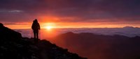 Silhouetted hiker standing on mountain ridge at golden sunrise, overlooking vast valley landscape with dramatic orange and purple sky, adventure and exploration concept.