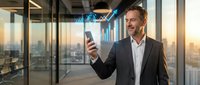 Middle-aged Caucasian businessman in suit using smartphone with holographic data visualization in modern office overlooking city skyline at sunset.
