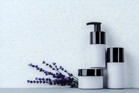 Minimalist white skincare cosmetic containers with lavender flowers on light textured background, natural beauty product packaging concept.