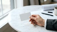 Caucasian male professional holding blank white business card at marble desk with papers and coffee cup, suitable for corporate branding and business identity mockups.