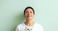 Young woman with short dark hair and East Asian ethnicity wearing white t-shirt with cat graphic, eyes closed, smiling peacefully against soft green background for lifestyle and portrait use.