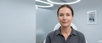 Professional middle-aged Caucasian female doctor in medical scrubs standing confidently in modern hospital operating room with surgical lighting equipment.