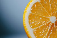 Fresh orange slice macro photography showing detailed pulp texture and juicy segments against blurred blue background, vibrant citrus fruit closeup.