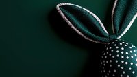 Elegant green fabric bunny ear with polka dot pattern on dark background, creating minimalist Easter decoration.