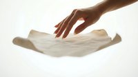 Hand reaching toward floating white fabric cloth against clean background for textile and fashion design concepts.