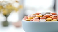 Colorful pastel macarons in soft pink, orange, and white arranged in ceramic bowl against light background, selective focus creates dreamy atmosphere.