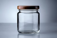 Empty glass jar with wooden lid on gray background, minimalist composition showing transparency and reflection. Clean container for food storage.