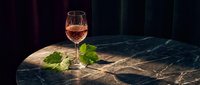 Elegant rosé wine glass on luxurious marble surface with fresh grape leaves, perfect for wine tasting, dining and hospitality marketing materials.