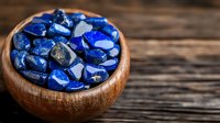 Vibrant blue lapis lazuli stones in wooden bowl on rustic table background, natural healing crystals and gemstones for meditation and alternative medicine.