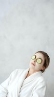 Young woman relaxing in white bathrobe with cucumber slices on eyes during spa treatment for skincare and wellness routine.