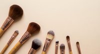 Professional makeup brushes set with natural bristles arranged on neutral beige background for beauty and cosmetics applications.