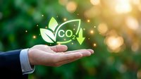 Businessman hand holding glowing CO2 reduction symbol with green leaves and arrow, representing carbon footprint decrease and environmental sustainability.