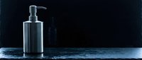 Stainless steel soap dispenser on marble surface against dark background for modern bathroom and kitchen design applications.