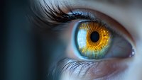 Extreme macro photography of amber colored human eye with detailed iris pattern and long eyelashes against blue background, showing intricate eye structure.