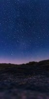 Starry night sky over dark rocky terrain with purple and blue gradient horizon, bright stars scattered across deep blue celestial atmosphere.