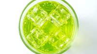 Top view of a refreshing green cocktail with ice cubes in a glass, isolated on white background. Vibrant lime drink for menu or bar design.