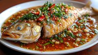 Steamed whole fish with soy sauce, ginger and scallions in traditional Chinese style preparation served on white plate for authentic Asian cuisine dining.