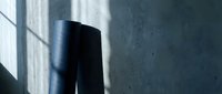Black cylindrical object casting dramatic shadow on textured concrete wall with natural window light creating geometric patterns for modern design.