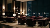Luxury hotel lobby lounge with leather armchairs and city night view through floor-to-ceiling windows creating elegant hospitality atmosphere.