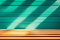 Diagonal shadows cast on turquoise wall with wooden deck floor creating minimalist geometric pattern and modern architectural abstract composition.