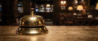 Vintage brass service bell on wooden counter in elegant hotel lobby with warm ambient lighting for hospitality and customer service concepts.
