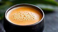 Fresh creamy espresso with delicate foam bubbles served in black ceramic cup against dark background, close up view with selective focus and condensation.
