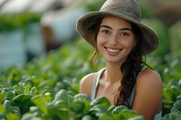 Young woman with long dark braid wearing sun hat smiles brightly while working in lush green garden on sunny summer day, natural lifestyle portrait.