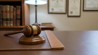 Wooden gavel and sound block on polished desk in professional law office with legal books and certificates on wall background for justice concepts.