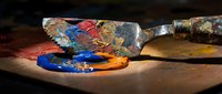 Artist palette knife covered in vibrant oil paints creating colorful smears on wooden surface for creative artwork and painting projects.