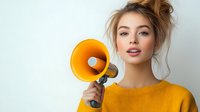 Young blonde Caucasian woman in yellow sweater holding orange megaphone for communication and announcement campaigns on white background.