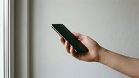 Hand holding modern smartphone with blank black screen against neutral wall background for mobile app mockup and digital communication concepts.