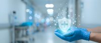 Healthcare professional in blue gloves holding digital shield icon with medical cross in hospital corridor, representing medical protection and safety.