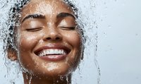 Young woman with radiant smile enjoying refreshing shower water cascading over her face, concept of skincare, hydration and natural beauty.