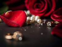 Red rose petals with diamond engagement ring and pearls on dark surface for romantic Valentine's Day wedding proposal celebration.