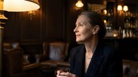 Professional businesswoman in elegant black blazer sitting thoughtfully in upscale restaurant with warm ambient lighting and bokeh background.
