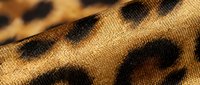 Closeup of leopard print fabric with brown and black spots on textured woven material, suitable for fashion, textile, and design projects.