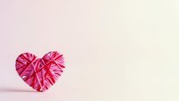 Pink yarn heart on soft pastel background for Valentine's Day crafts and romantic decorations with copy space.