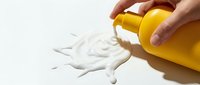 Caucasian hand pouring white liquid from yellow bottle onto white surface, depicting product application or spillage for cosmetic, cleaning or industrial use.