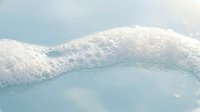 Soft white foam bubbles floating on calm turquoise water surface creating peaceful spa-like atmosphere for wellness and relaxation concepts.